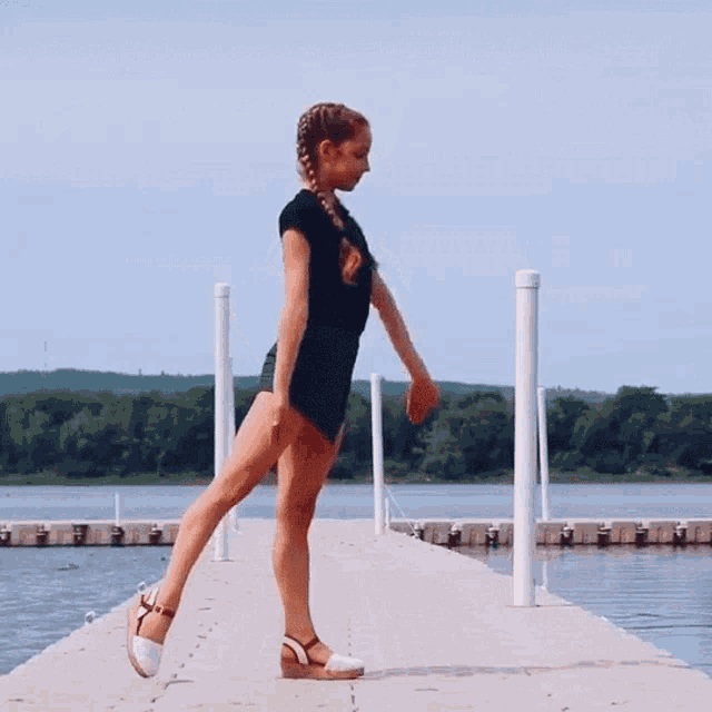 a woman in a black dress is standing on a dock overlooking a body of water