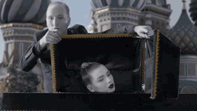 a man in a suit is holding a box with a woman 's head inside of it