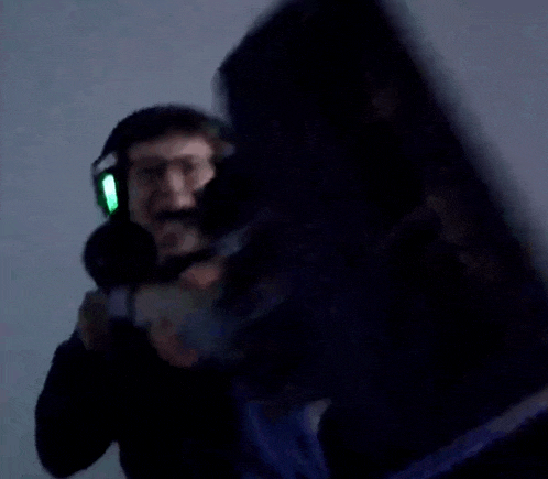 a man wearing headphones is holding a microphone in a dark room while another man is holding a shield .