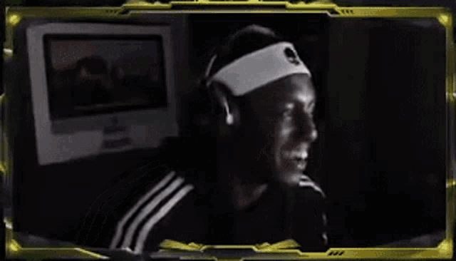 a man wearing headphones and a headband is smiling in front of a computer monitor .