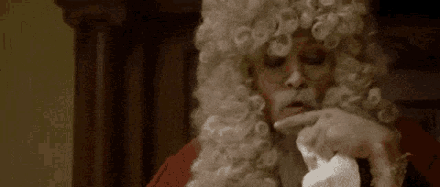 a man in a wig is blowing his nose while wearing glasses .