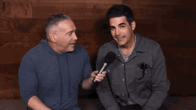 two men are sitting next to each other and one is holding a microphone in his hand
