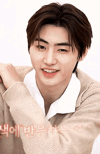 a young man wearing a tan sweater and a white shirt is smiling