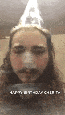 a man with long hair and a beard is wearing a birthday hat and smoking a cigarette .