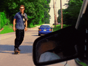 a man is riding a skateboard down a street with a blue car behind him