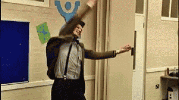 a man in a suit and suspenders is dancing in a classroom with his arms in the air .
