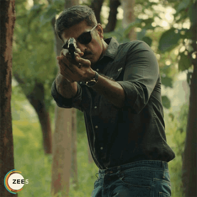 a man holding a gun with a zees logo in the background