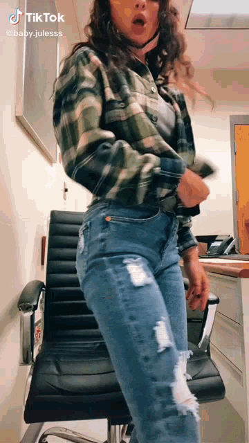 a woman in a plaid shirt and ripped jeans is standing in front of a black chair .