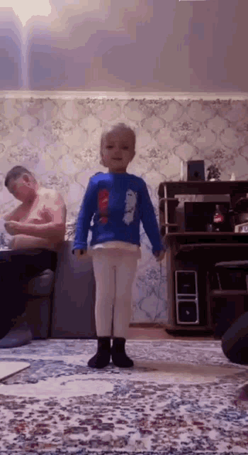 a little girl is standing in a living room with a man sitting on a couch .