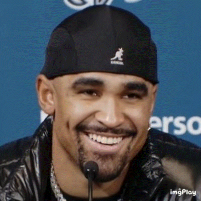 a man with a beard is smiling while wearing a black hat and jacket .