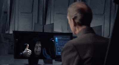 a man in a suit looks at a screen with a picture of a man giving the thumbs up