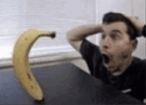 a man is sitting at a table with his mouth open and a banana in the background .
