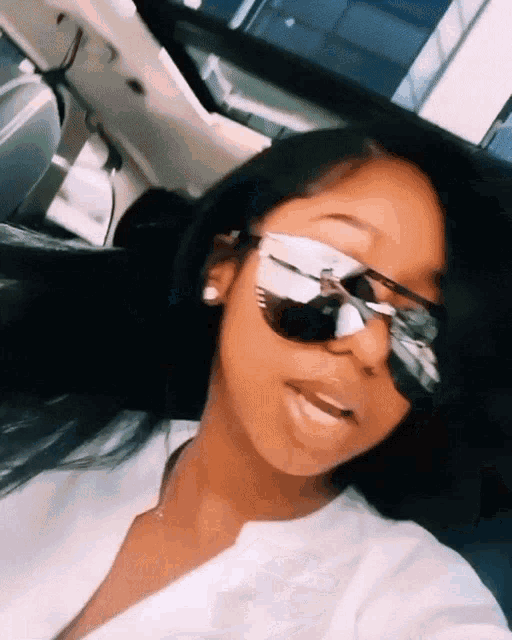 a woman wearing sunglasses and a white shirt is taking a selfie in a car .