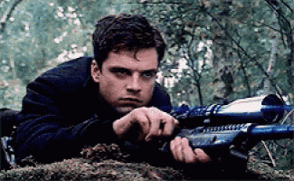 a man is laying down holding a sniper rifle in the woods .