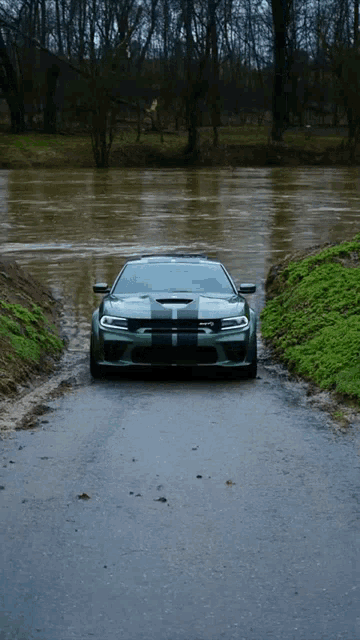 a green car is driving down a road next to a body of water
