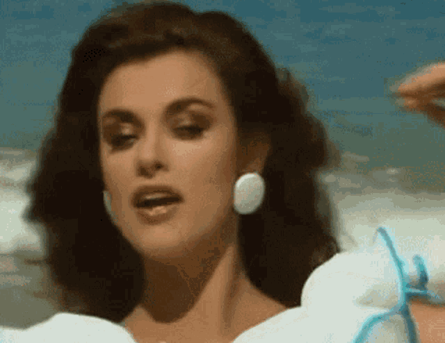 a woman wearing a white dress and white earrings looks at the camera