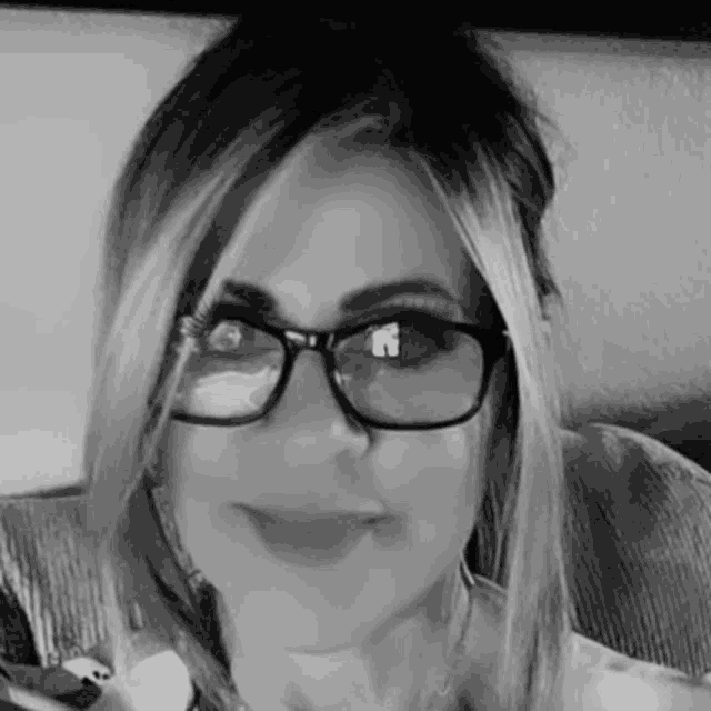 a woman is wearing glasses and smiling in a black and white photo .
