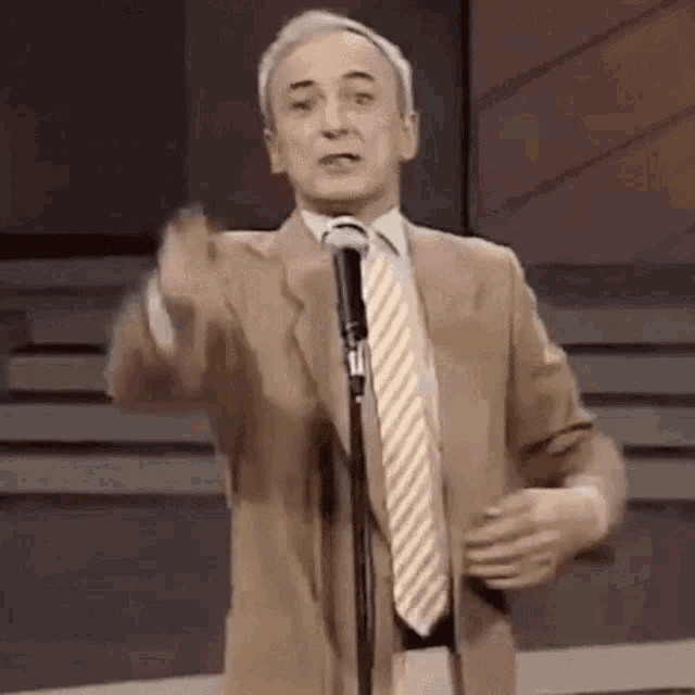 a man in a suit and tie is speaking into a microphone .