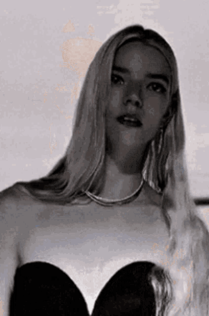 a black and white photo of a woman wearing a black strapless dress and a necklace .