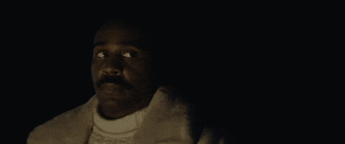 a man with a mustache is standing in the dark looking up .