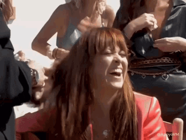 a woman in a red jacket is laughing in a group of people