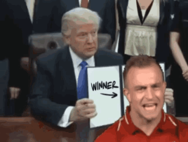 a man in a red shirt holds a sign that says winner