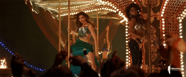 a woman in a green top is dancing on a merry go round in front of a crowd of people