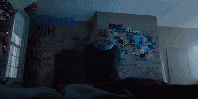 a person sitting on a bed in a room with graffiti on the walls including the word shame