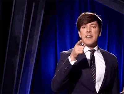 a man in a suit and tie is standing in front of a blue curtain with his hands in his pockets .