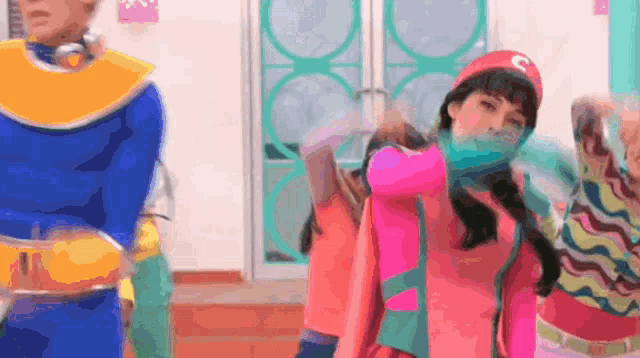 a woman in a pink dress is standing next to a man in a blue costume with the letter c on his hat .