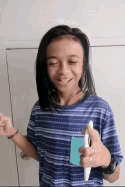 a young girl in a blue striped shirt holds a pen and a piece of paper