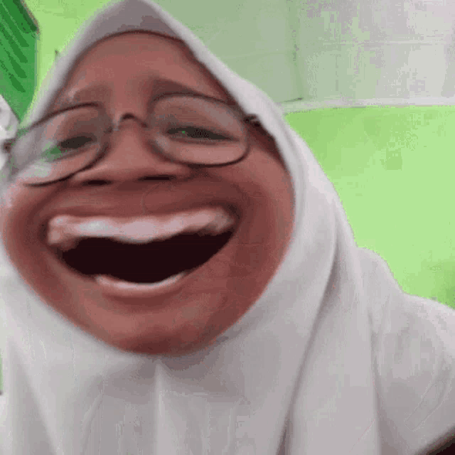 a woman wearing glasses and a hijab is smiling with her mouth open .