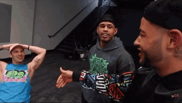 a man wearing a blue tank top with the word god on it talks to two other men