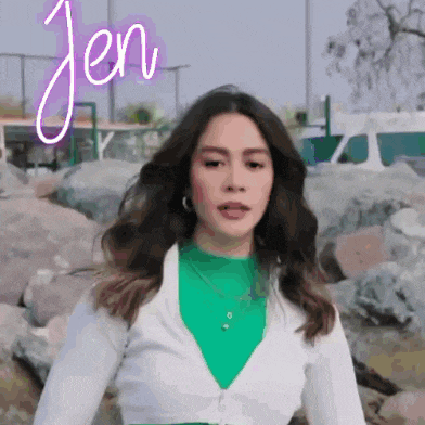 a woman wearing a green sweater and a white jacket is standing in front of a rocky area .