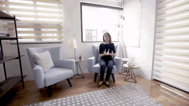 a woman sits in a chair in front of a window with blinds