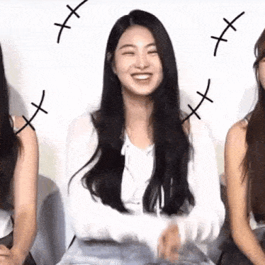 a woman with long black hair is smiling while sitting next to a group of women .