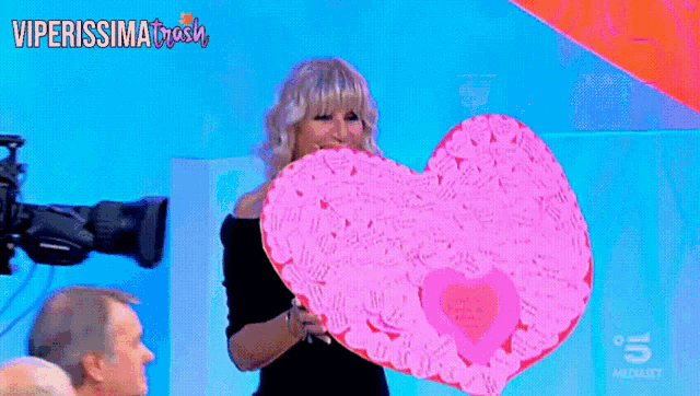 a woman is holding a large pink heart with the words viperissima trash on the bottom right