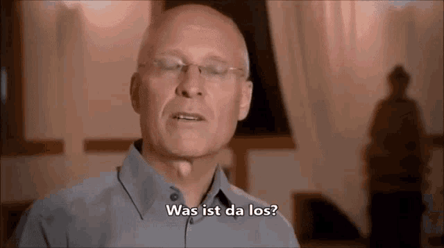 a bald man wearing glasses says " was ist da los " in german
