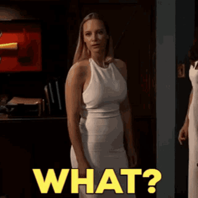 a woman in a white dress is standing in front of a sign that says " what "