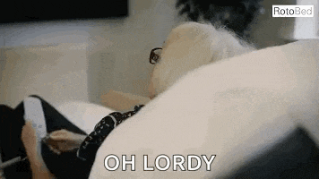 an elderly woman is sitting on a couch with a remote control in her hand and says `` oh lordy '' .