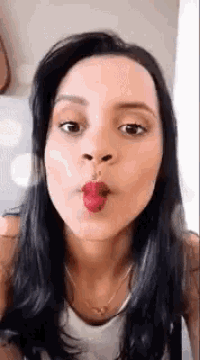 a woman with long dark hair is blowing a kiss with red lipstick .