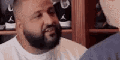 a man with a beard is talking to another man in front of a shelf full of shoes .