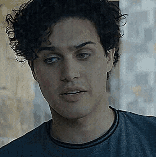 a close up of a man 's face with curly hair wearing a gray shirt .