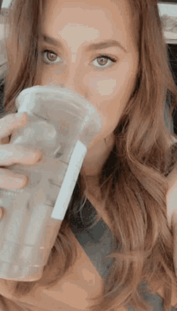 a woman is drinking from a plastic cup with a label that says ' starbucks ' on it