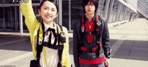 a man and a woman are standing next to each other in front of a building . the woman is wearing a yellow jacket .