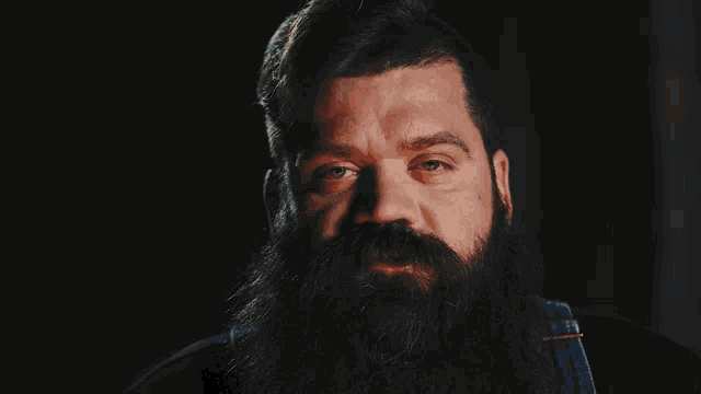 a man with a long beard and overalls looks at the camera