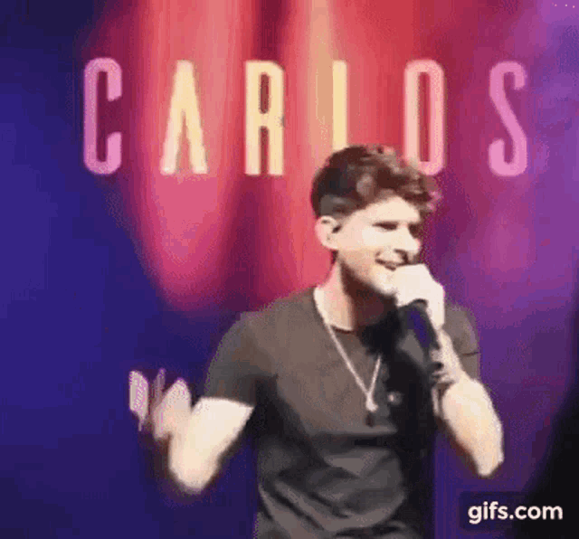 a man is singing into a microphone on a stage in front of a red curtain .