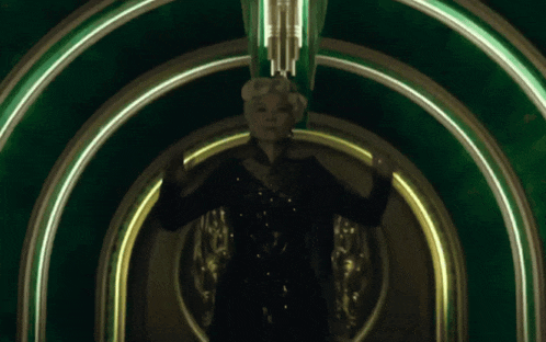 a woman in a black dress is standing in a green archway