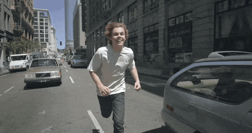 a young man is running down a street with a building that says new loading in the background
