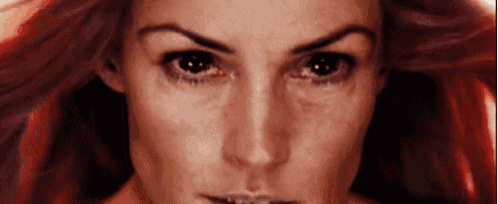 a close up of a woman 's face with red hair looking at the camera .
